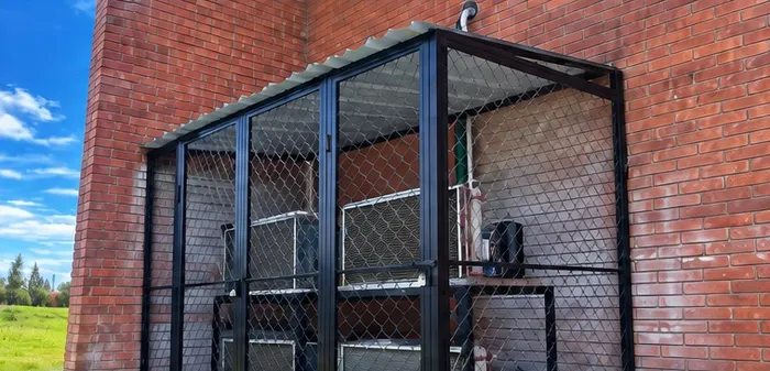 Jaula metálica fabricada a la medida junto a muro de ladrillo